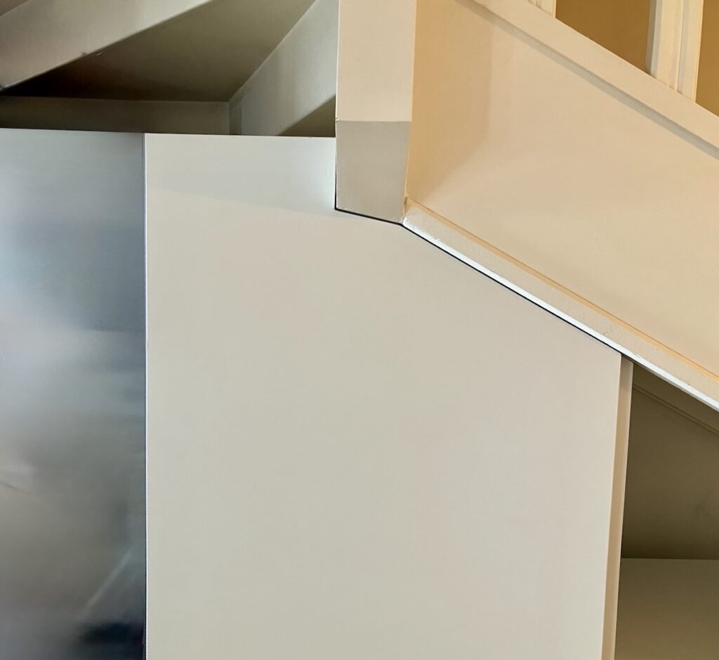 Détail du tablettage minutieux d'une porte sur mesure, intégrant une poutre sous un escalier