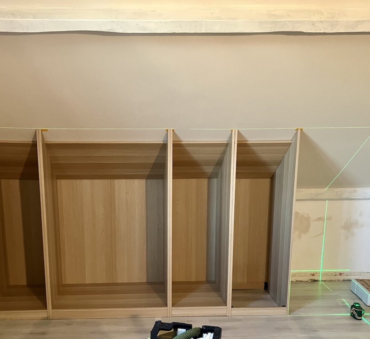 Ajustage des caissons de dressing sous pente avec un niveau laser afin d'obtenir un alignement parfait malgré les irrégularités de la charpente, du sol et des murs.